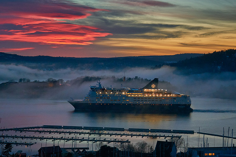 A marine cruise ship sails at dusk on a Norwegian fjord